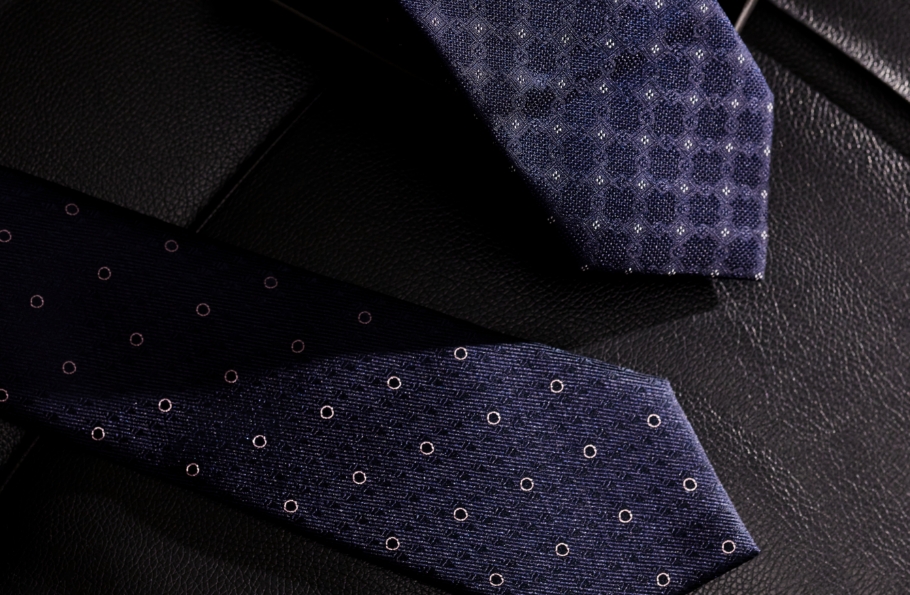 Dwa granatowe krawaty Bytom, leżące na czarnej skórzanej kanapie.