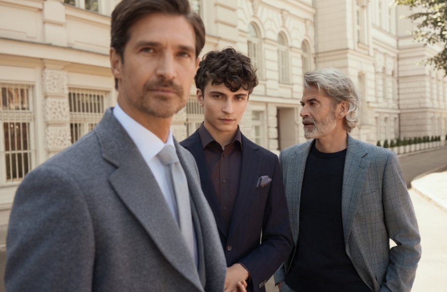 Trzech mężczyzn w różnym wieku, stojący przed budynkiem, w garniturach