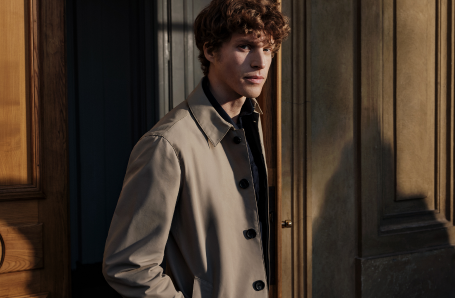 Mężczyzna w beżowym płaszczu Bytom na tle drewnianej ściany.