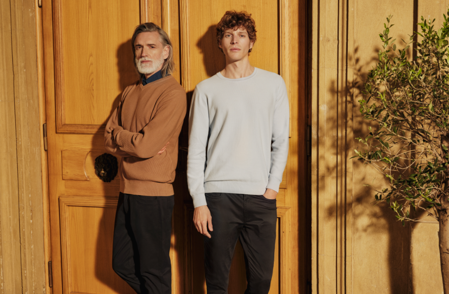 Dwóch mężczyzn stojących przy drewnianych drzwiach, ubranych w wiosenne stylizacje Bytom.