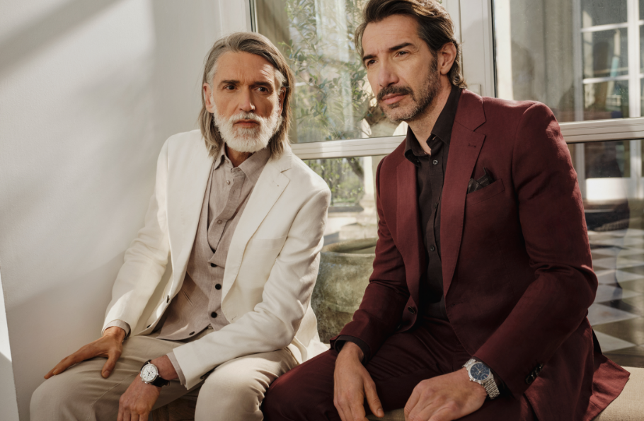 Dwóch dojrzałych mężczyzn w garniturach Bytom siedzących przy oknie z widokiem na werandę.