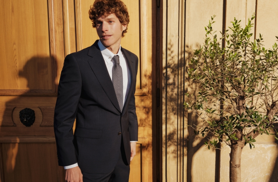 Mężczyzna w garniturze Bytom, stojący na patio przy drzewku oliwnym.